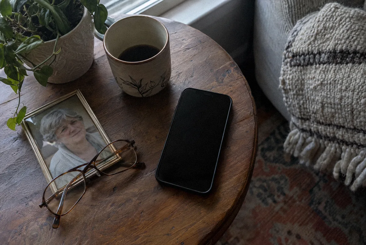 A phone with a dark screen beside reading glasses and a framed photograph
